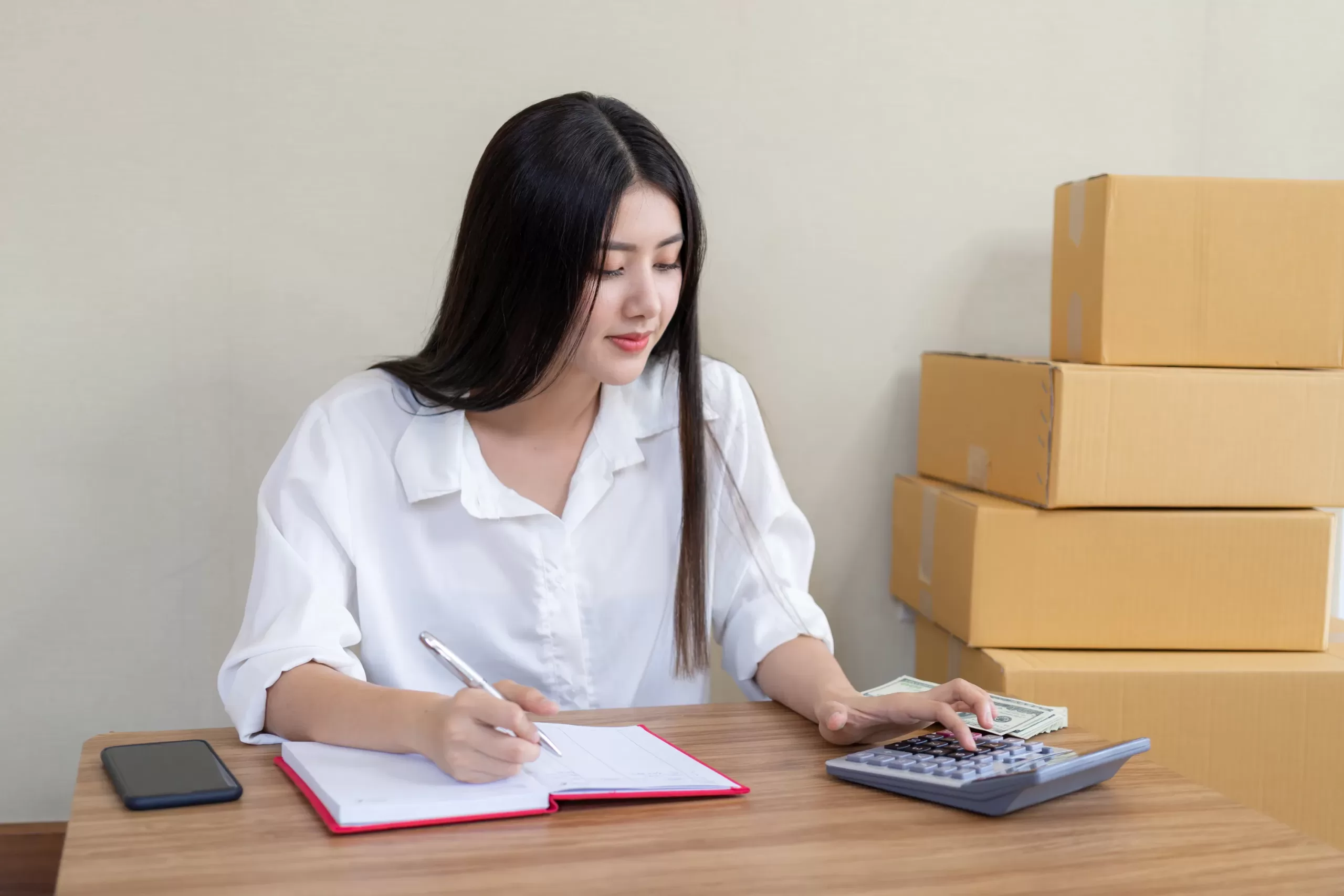 how to reduce packaging cost - a woman calculating cost with boxes behind her